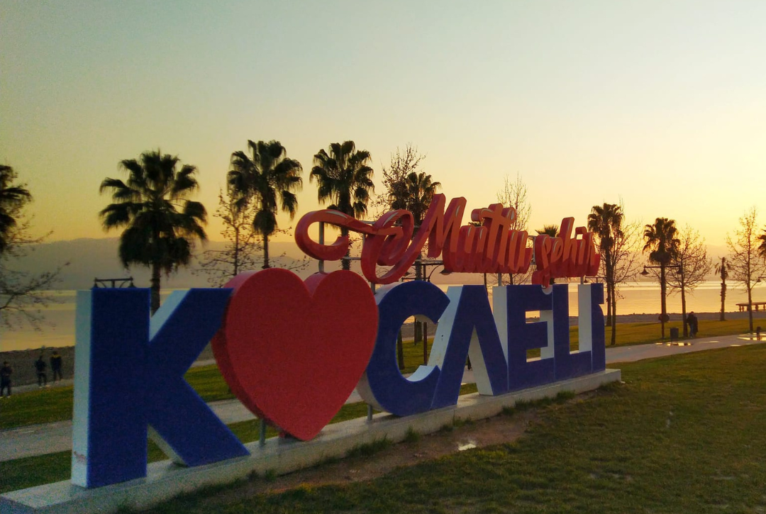 The "I Love Kocaeli" sign at the waterfront during sunset, with mountains and trees in the background.